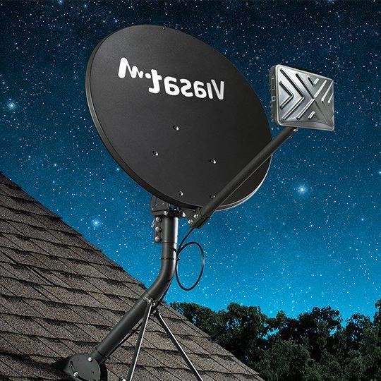 Gray fixed broadband terminal with TRIA and a white Viasat logo, mounted to the roof of a house against a starry night sky