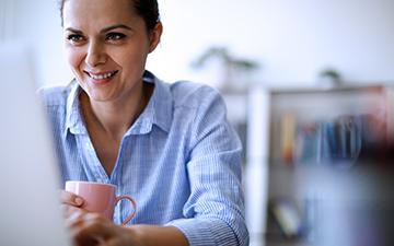 女人坐在电脑前，喝着咖啡，面带微笑